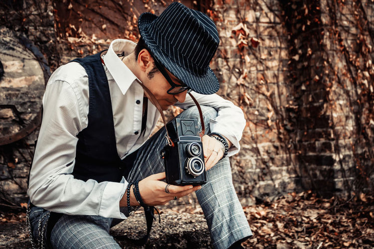 Retro-styled man taking picture with vintage medium format photo camera outdoors.
