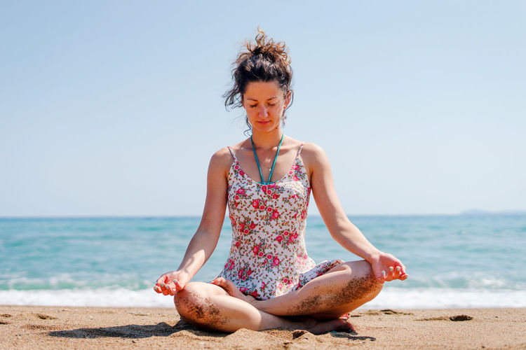 Full length of woman meditating while sitting at beach