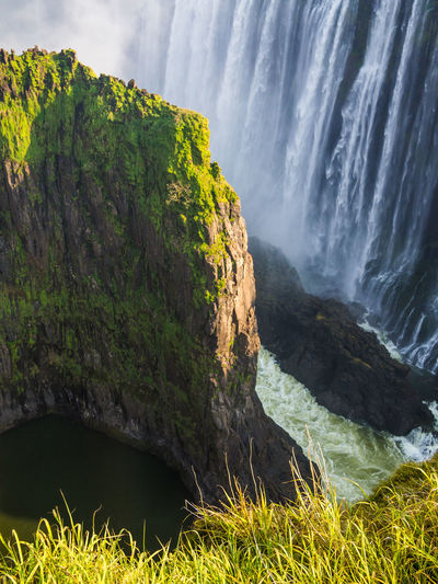 Scenic view of victoria falls waterfall with overgrown cliff and green grass, zambia 