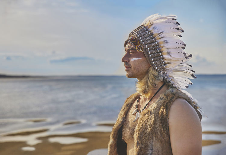 A man in traditional native american clothing near the sea