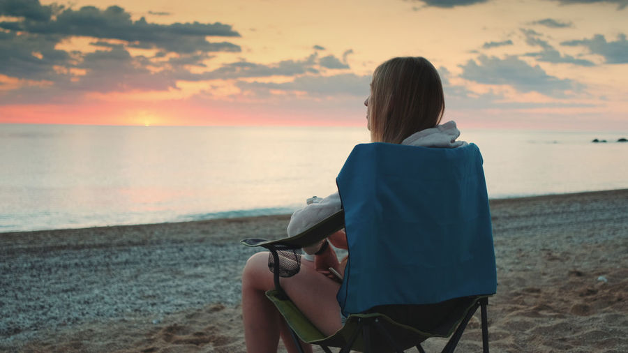 Rear view of woman sitting on beach during sunset