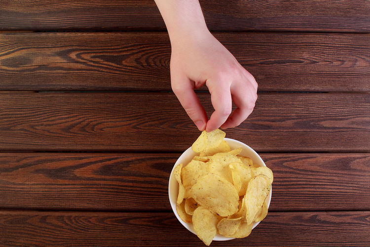 Hand holding potato chips on dish isolated on wooden background