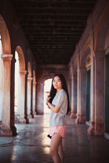Portrait of smiling young woman standing in corridor of building