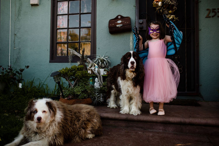 Young girl in dress up standing on porch with dogs