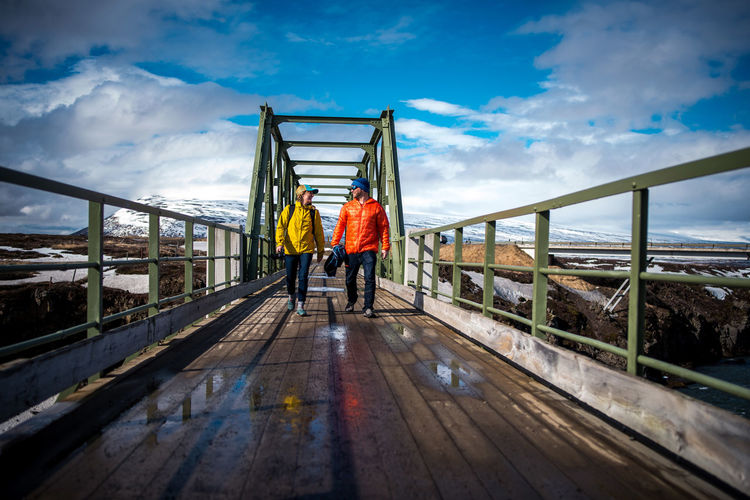 Man and woman in jackets walking across bridge in iceland