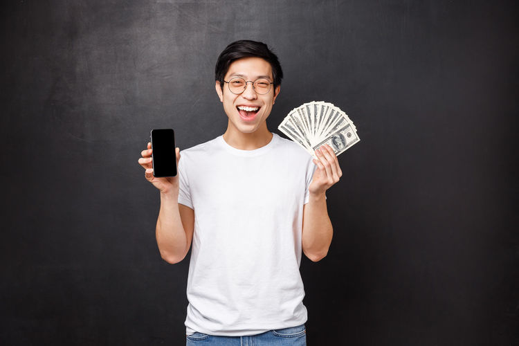 Man holding smart phone and cash against black background