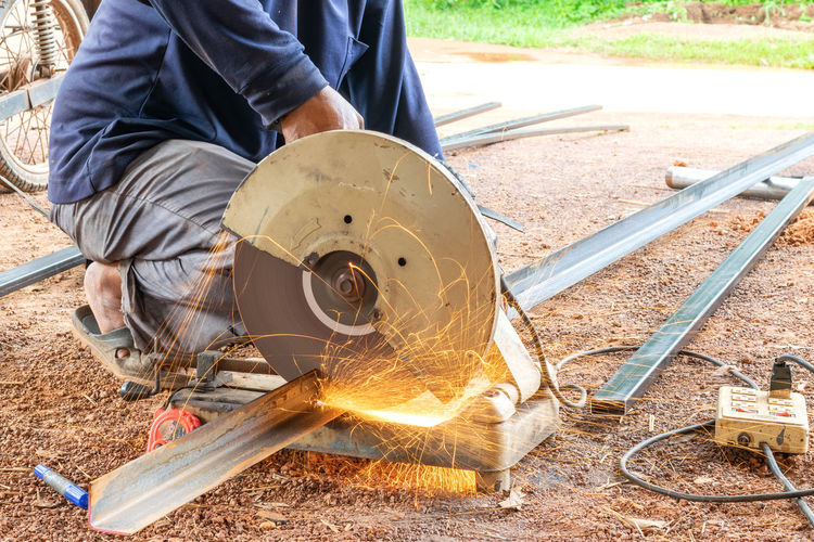 Low section of man cutting metal with circular saw at construction site