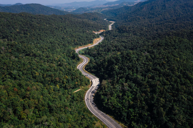 Long road curved in valley connecting countryside in the rainforest and the verdant hill forest 