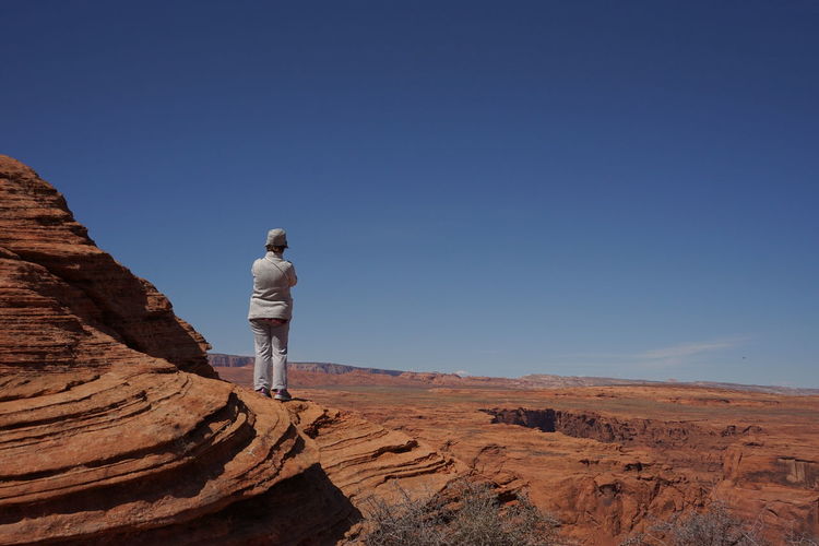 Rear view of man standing on rock against clear blue sky