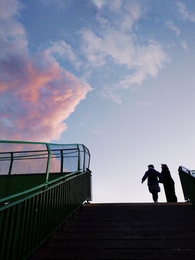 Low angle view of silhouette people standing on railing against sky
