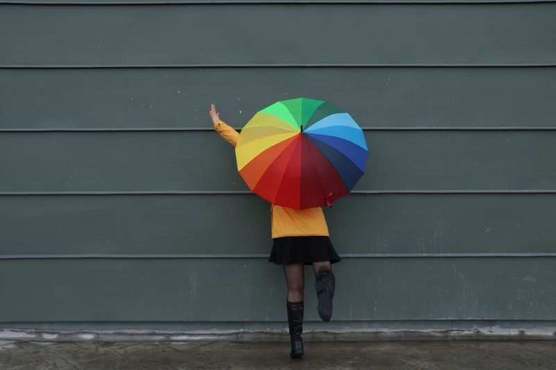 Woman holding umbrella while standing against wall