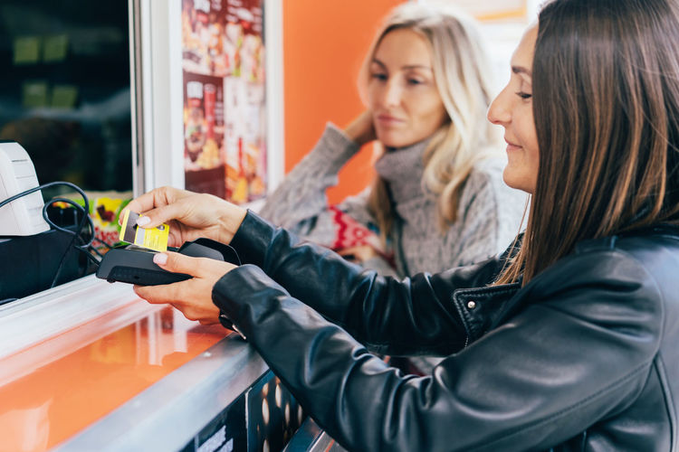 Two attractive girlfriends buying fast food and paying in eat market in the street.