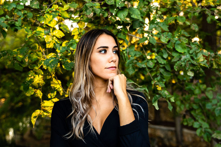 Beautiful woman with dyed hair looking away while standing amidst plants