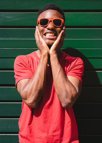 Smiling young man wearing sunglasses standing against wall
