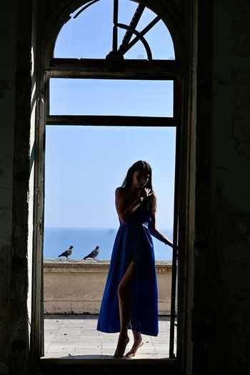 Woman standing by window against blue sky