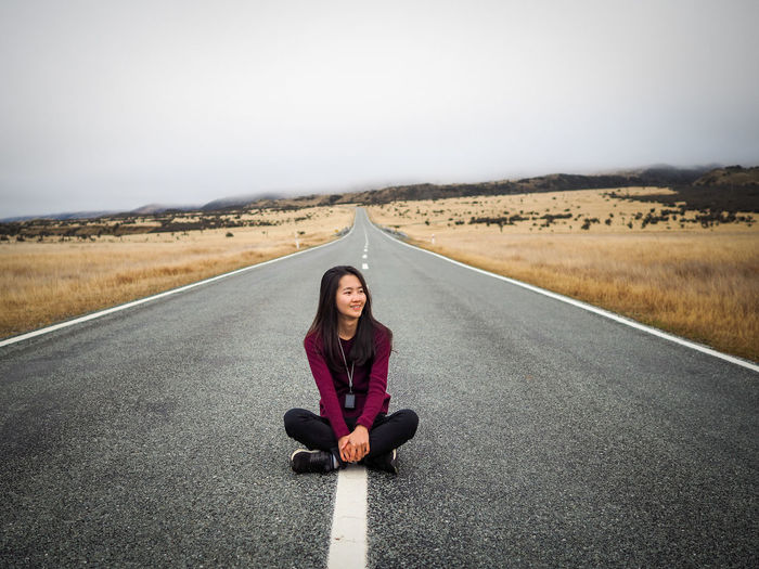 Portrait of woman sitting on road against sky