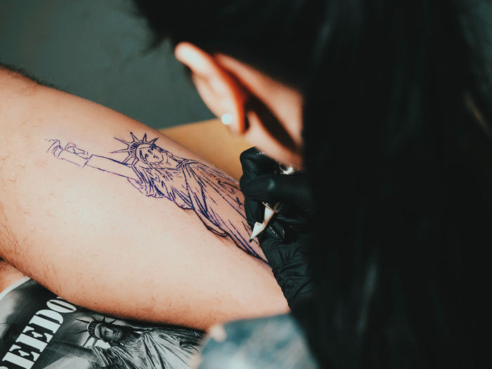Young woman tattooing statue of liberty man on calf at parlor