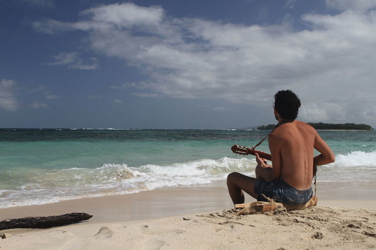Rear view of man playing ukelele at the beach
