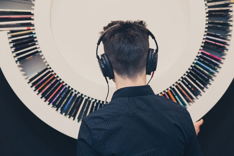 Rear view of teenage boy listening music while standing against decoration