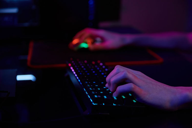 Professional gamer play computer video game in dark room, use neon colored rgb mechanical keyboard