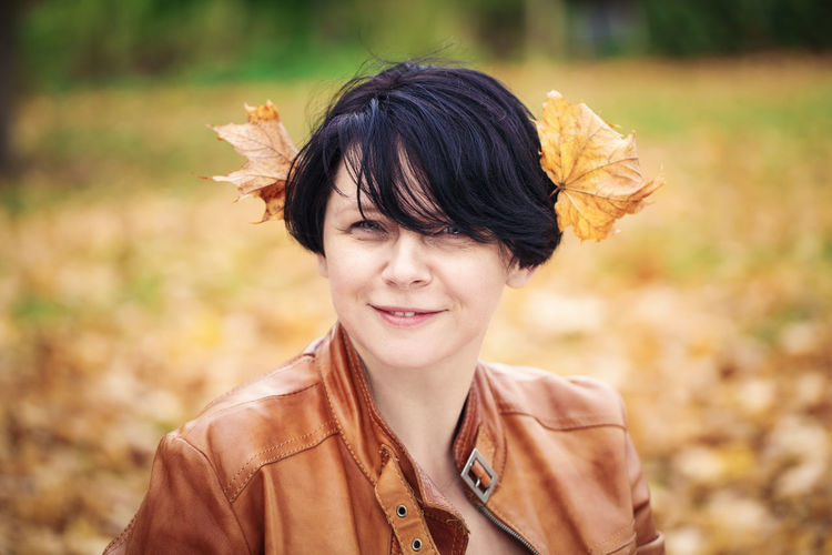 Portrait of smiling woman with autumn leaves on head