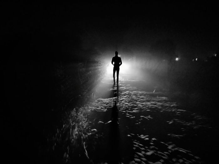 Silhouette man standing on illuminated lamp at night