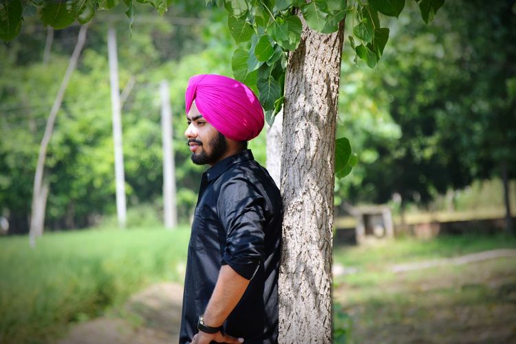 Side view of man wearing turban by tree on field