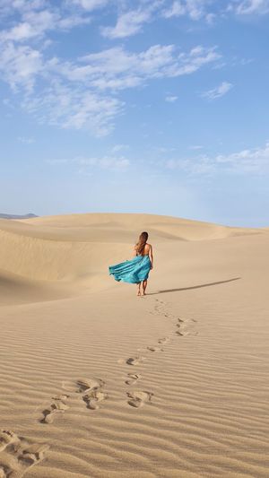 Woman with longdress on sand dune in desert against sky