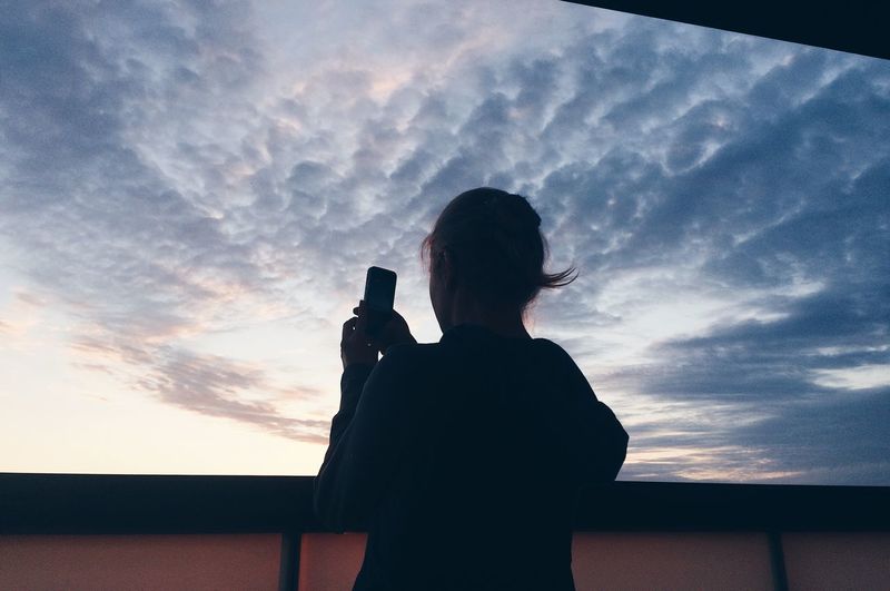 Silhouette of woman using smart phone against sky