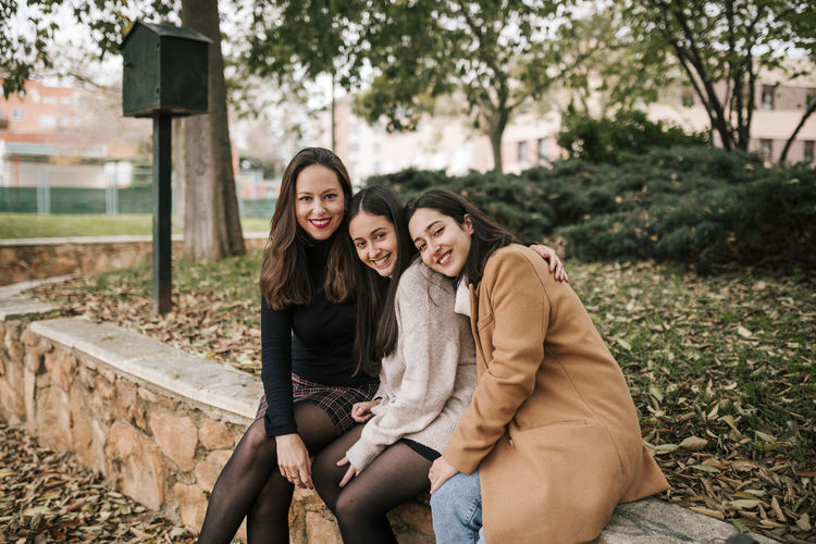 Smiling mature woman with daughters sitting on retaining wall in park