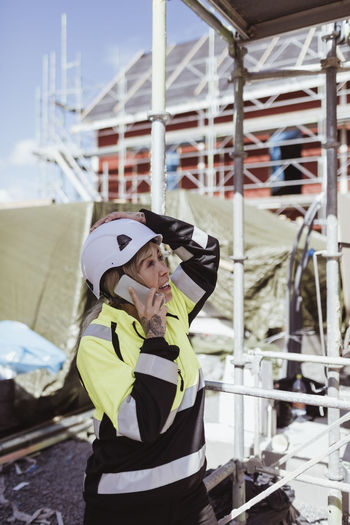 Female builder talking on mobile phone standing at scaffolding