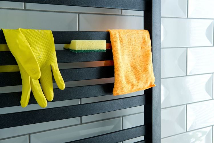 Basic house cleaning equipment - rubber glove, microfiber cloth and a spong hung on bathroom heater