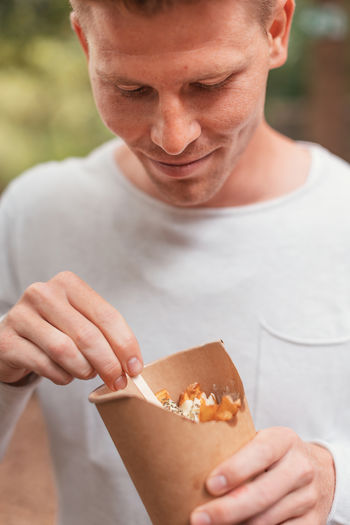 Young man holding a foil of french fries and mayonnaise