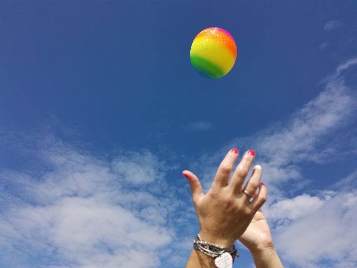 Cropped hands catching ball against cloudy sky