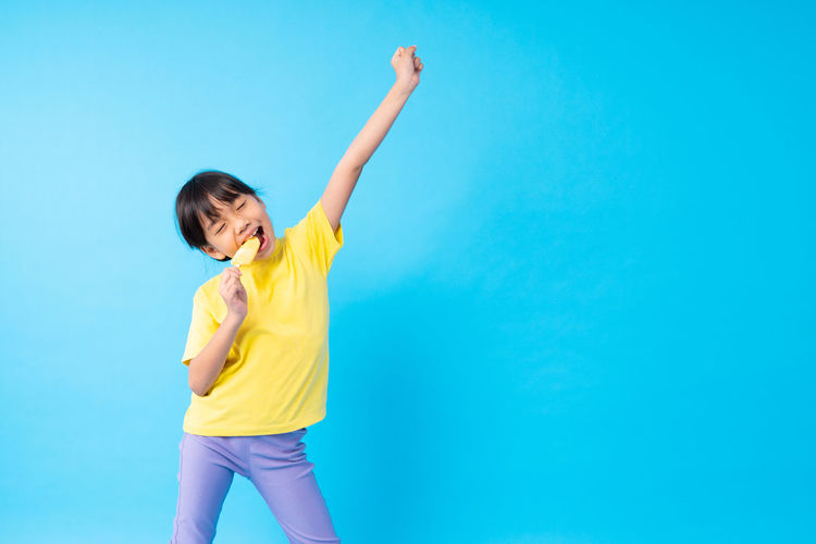 Girl eating popsicle while dancing against blue background