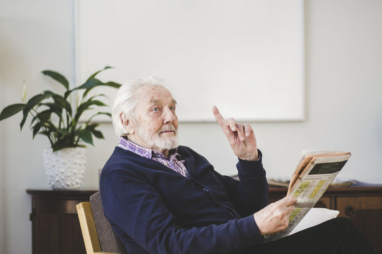 Senior man pointing while holding newspaper in nursing home