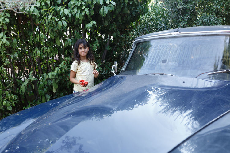 Girl watching next to blue car in the garden