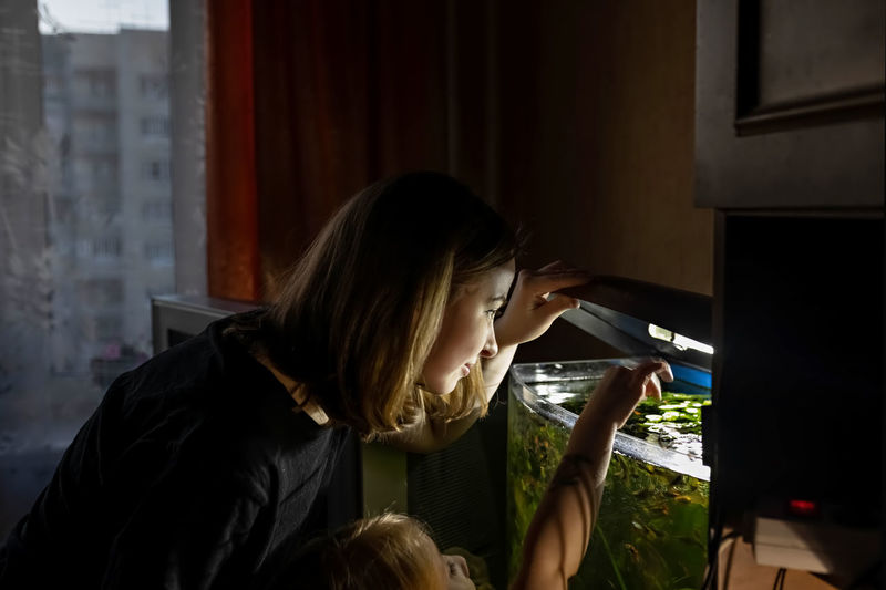 A young woman and a little girl feed fish in a home aquarium.