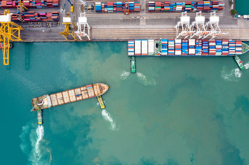 Aerial top view tugboat pushing container ship to commercial port load and unloading of goods 