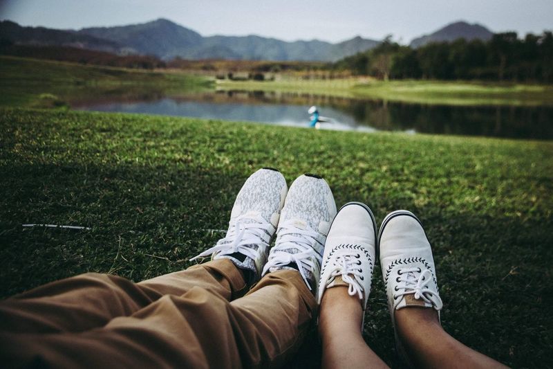 Low section of couple wearing shoes while sitting at lakeshore