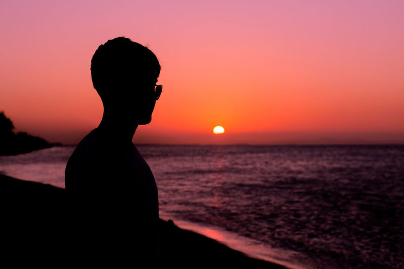 Silhouette man looking at sea against sky during sunset