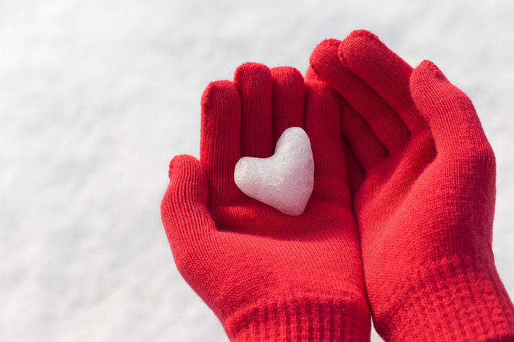 Close-up of hand holding red heart shape on snow
