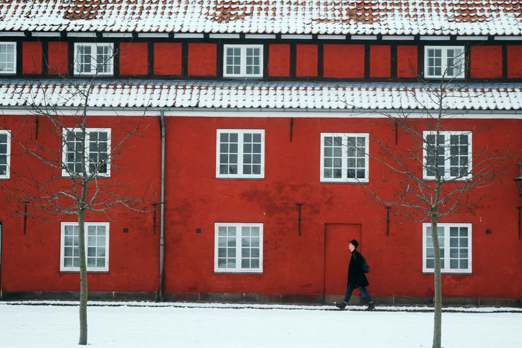 Side view of man walking against building in city during winter
