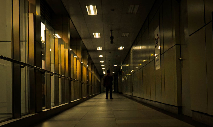 Rear view of man walking on illuminated corridor of building