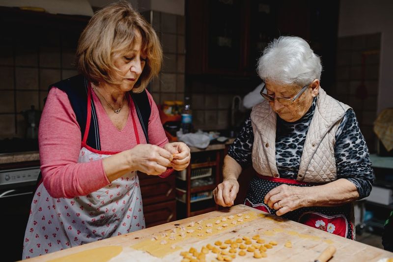 Busy senior women standing at table and preparing traditional domestic tortellini for dinner at home