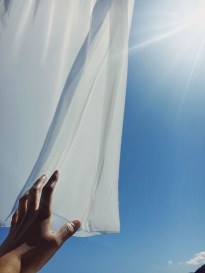 Cropped hand reaching textile against sky