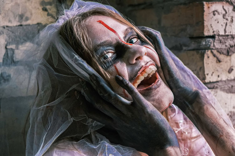 Zombie woman dead bride looks into camera and laughs nervously, making sudden movements. 