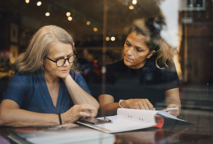 Businesswoman discussing with female coworker over smart phone at clothing store