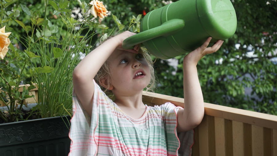 Girl looking into watering can while standing by railing at yard