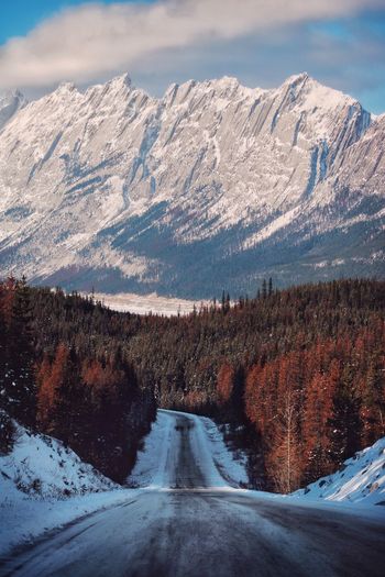 Snow covered road by snowcapped mountains against sky